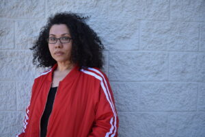 Headshot of a feminine Black woman with curly hair, glasses, and a red jacket