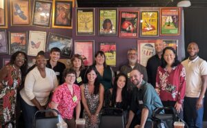A group of people smile in front of a background of theater posters
